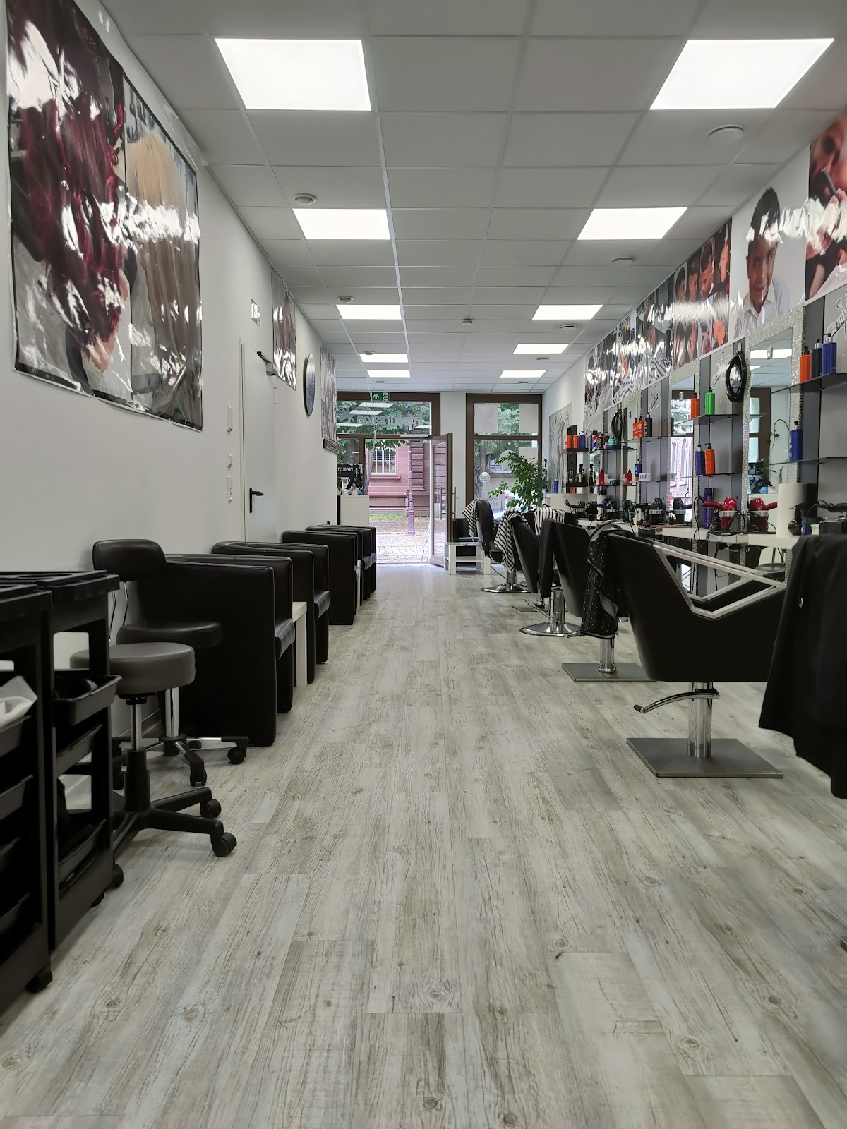 Blick durch den Salon: links die Wartesessel, rechts die Bedienplätze mit Spiegeln, dazwischen der helle Holzboden bis zur Eingangstür.
